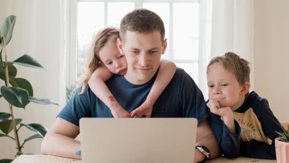 Ein Mann arbeitet vor einem Laptop mit zwei Kindern
