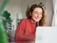 Eine lächelnde Frau sitzt vor einem Laptop mit einem Stift