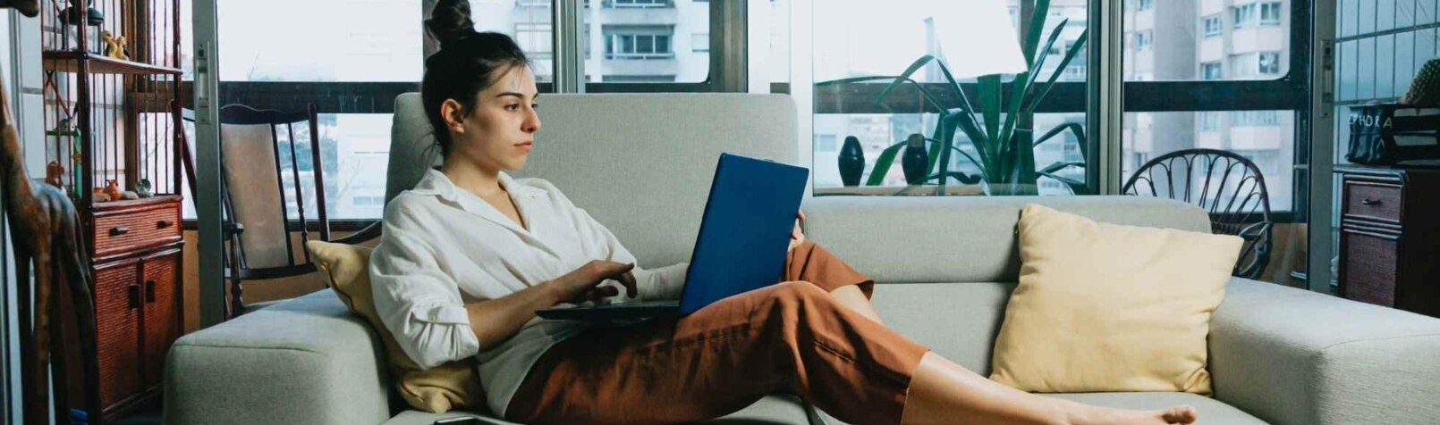 Eine Frau liegt auf einem Sofa und arbeitet mit einem Laptop.