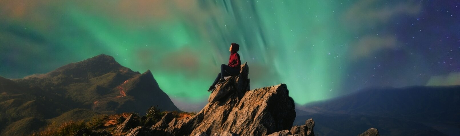 Person sitz auf einem Felsen und beobachtet Nachthimmel
