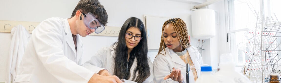 Drei Schüler in Laborkitteln führen ein Chemie-Experiment durch.