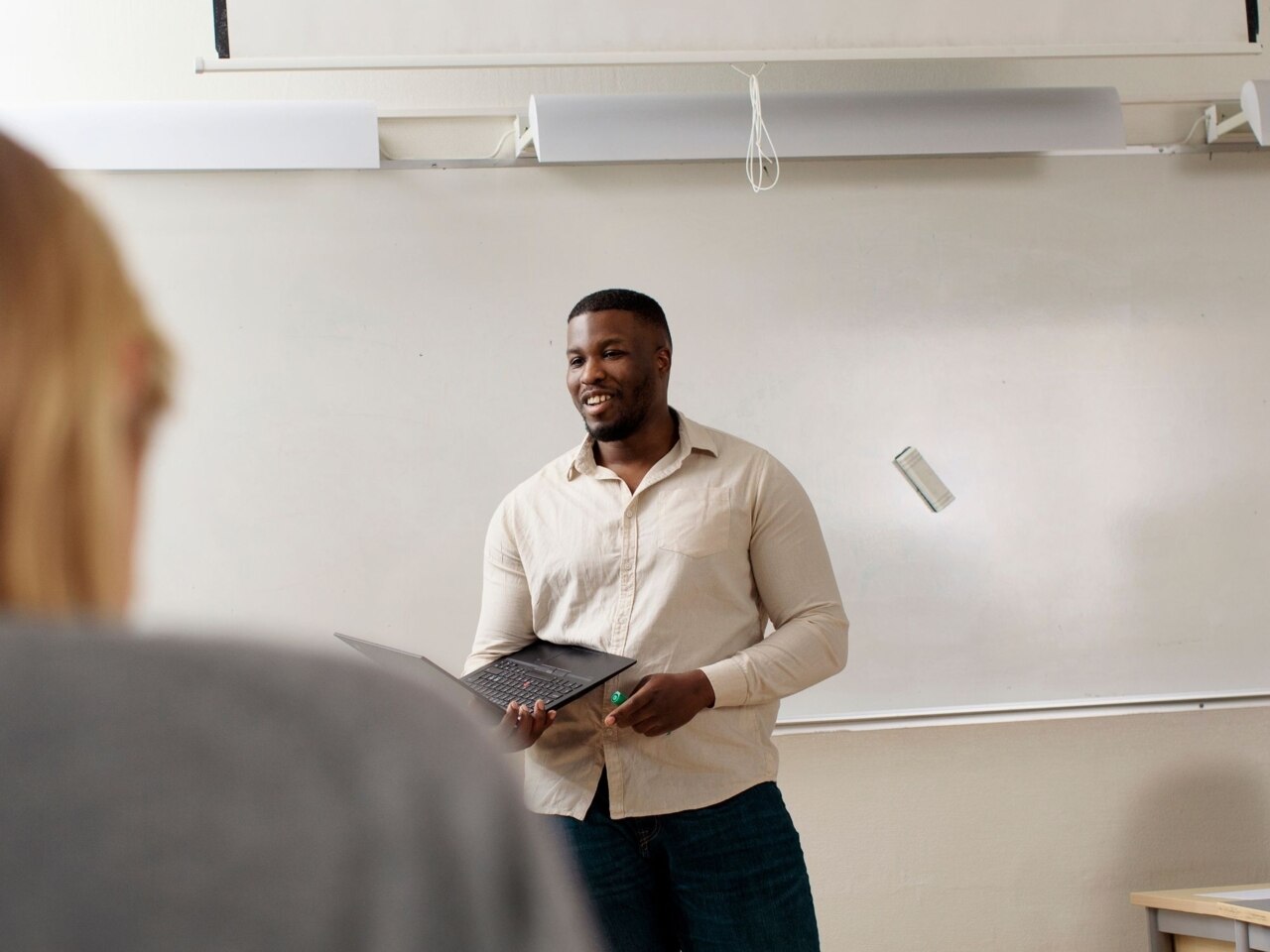 Mann steht vor einem Whiteboard und hält einen Laptop in der Hand.