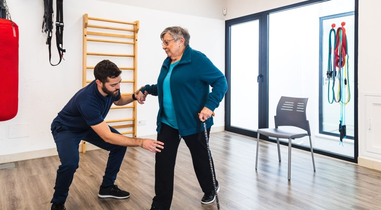 Männlicher Ausbilder unterstützt eine alte Frau beim Trainieren im Fitnessstudio