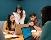 Gruppe von Mitarbeiter*innen am Schreibtisch, blicken zusammen auf Laptops.