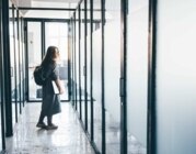 Eine junge Frau mit Laptop und Rucksack verlässt ein Bürogebäude.