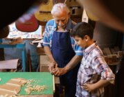 Ein älterer Mann bringt einem Jungen in einer Werkstatt den Instrumentenbau bei