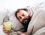 Müde aussehender Mann liegt mit einem Getränk im Bett