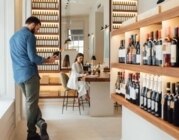Ein Sommelier steht in einem Weingut und liest das Etikett einer Weinflasche. Er arbeitet mit einer Geschäftsfrau zusammen.