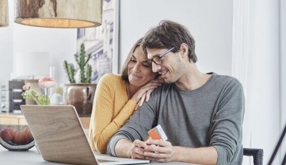 Ein Mann und eine Frau sitzen lächelnd mit Kreditkarte in der Hand vor einem Laptop.
