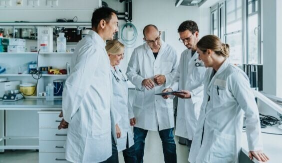 Ein Gruppe von Wissenschaftler*innen im Labor beugt sich über ein Tablet