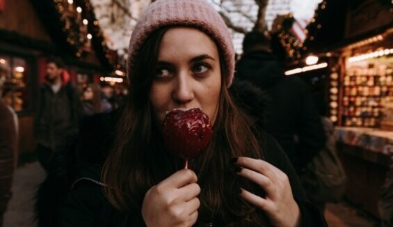 Eine Frau auf einem Weihnachtsmarkt isst einen Liebesapfel