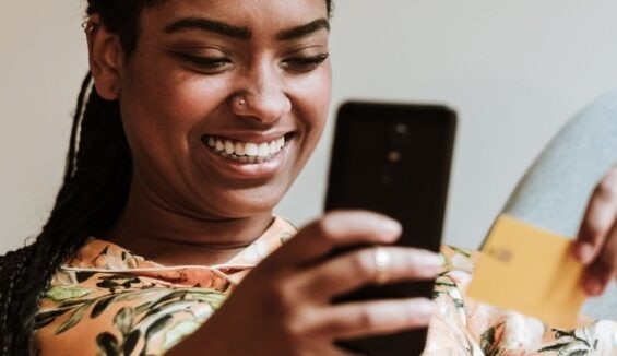 Lächelnde Frau mit Smartphone und Kreditkarte in der Hand