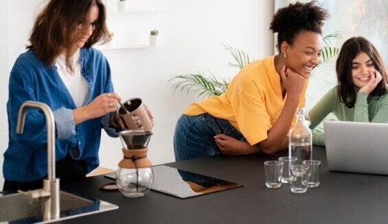Gruppe junger Frauen sitzt an Küchenzeile und arbeitet am Laptop