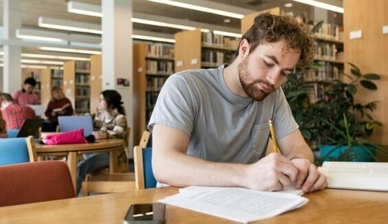 Ein junger Mann arbeitet in der Bibliothek an einem Text.