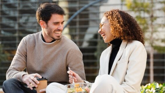 Ein Mann und eine Frau sitzen vor dem Büro im Grünen beim Mittagessen.