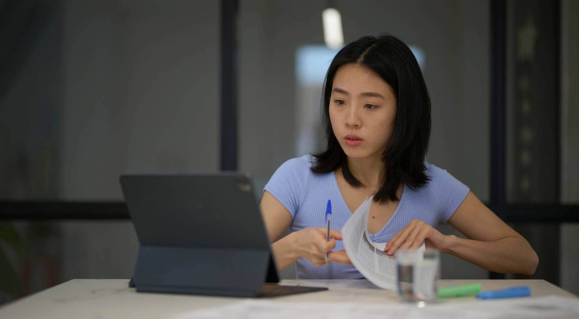 Eine Frau schaut auf ein Tablet und hält einen Stift und Zettel in der Hand.