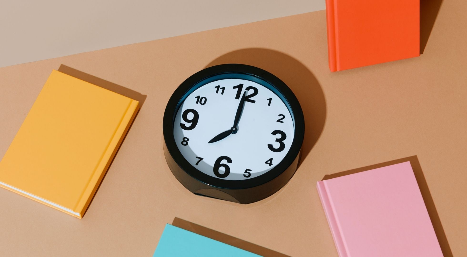 Eine Uhr und drumherum vier bunte Bücher.