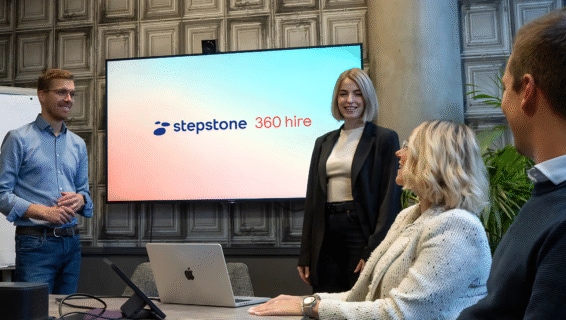 Zwei Kollegen stehen vor einem Bildschirm und präsentieren Stepstone 360 Hire anderen Kollegen