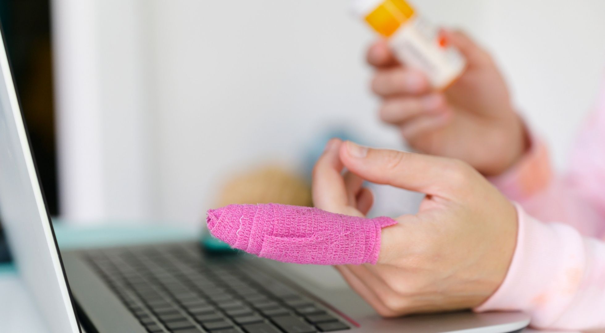 Nahaufnahme eines Fingers mit pinkem Verband über einer Tastatur.