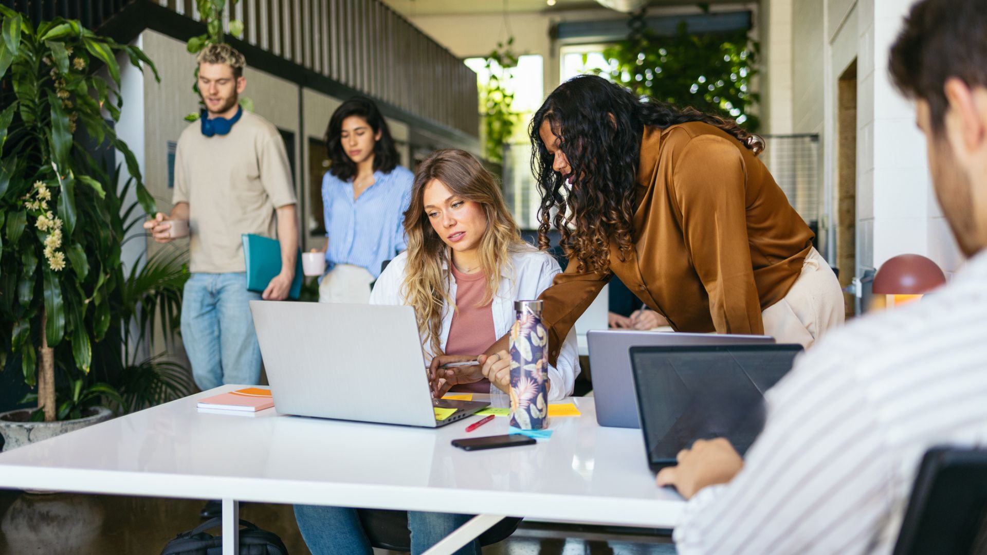 Eine Gruppe Mitarbeitender im Büro. Zwei von ihnen schauen auf einen Laptrop.