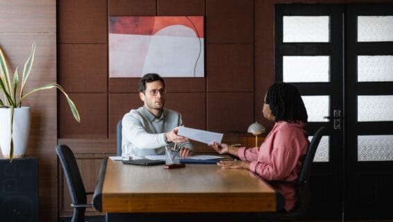 Ein Mann und eine Frau sitzen an einem Tisch und überreichen sich ein Blatt Papier.