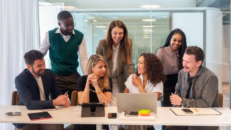 Eine gemischte Gruppe aus 7 Menschen lachen in einem Büroumfeld
