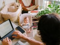 Eine Person arbeitet im Homeoffice und schaut ein Baby in einer Wiege an
