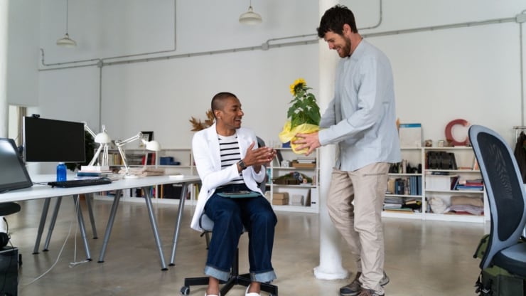 Ein Mensch überreicht stehend einem sitzenden Menschen ein Geschenk 
