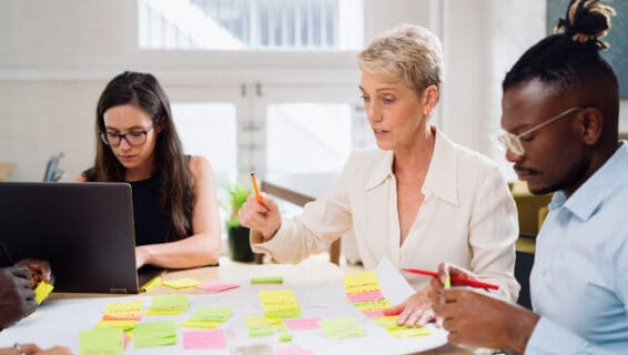 3 Personen sitzen am Konferenztisch und notieren Ideen auf bunten Post-its.