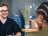 Stepstones Senior Talent Acquisition Manager Christopher Lennartz sitzt einer Frau mit Zöpfen gegenüber und lächelt sie an.