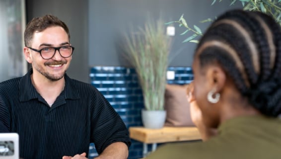 Stepstones Senior Talent Acquisition Manager Christopher Lennartz sitzt einer Frau mit Zöpfen gegenüber und lächelt sie an.
